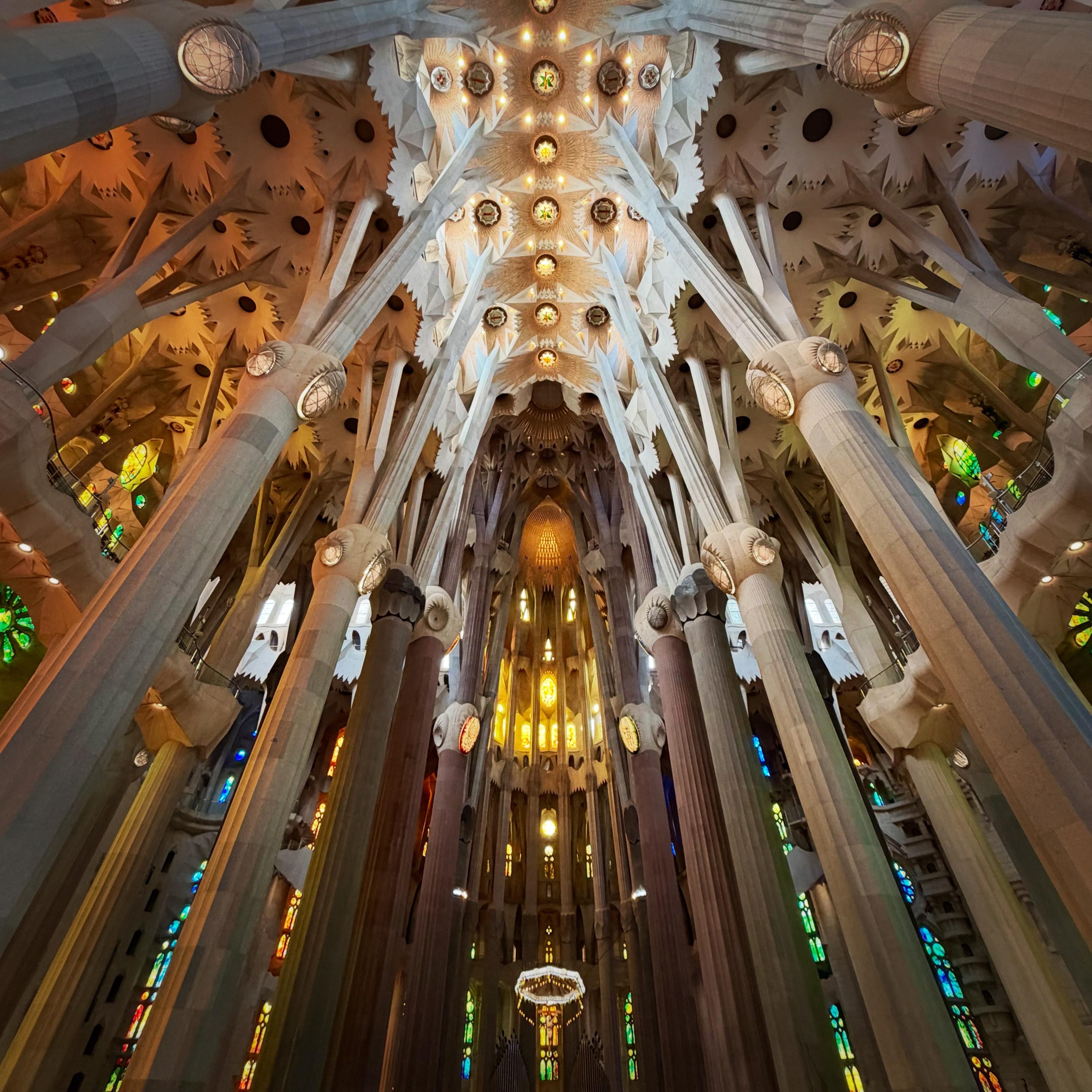The stunning interior of La Sagrada Família cathedral with towering columns, colourful stained-glass windows, and an intricately detailed, vaulted ceiling. Warm light illuminates the space, creating a majestic, ethereal atmosphere