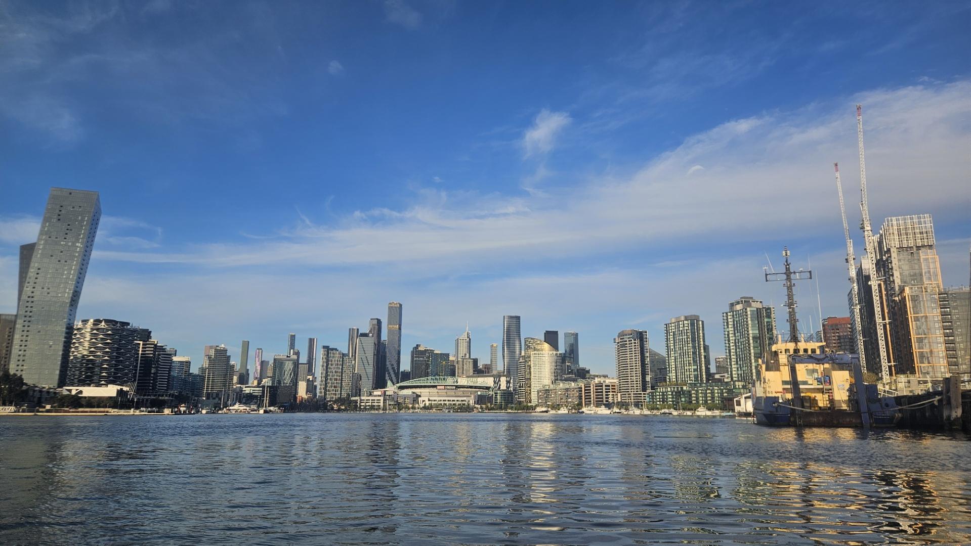 Photo of Docklands from under the Bolte Bridge, about 60% sky(with some wispy clouds), 20% cityscape, and 20% water.